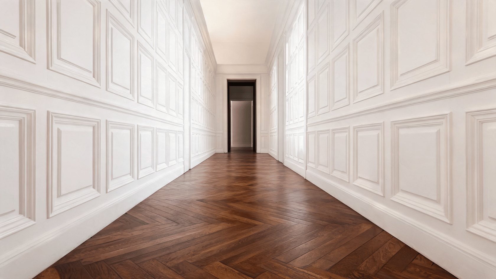 White wainscoting wall panels lining a hallway with dark wood herringbone flooring.