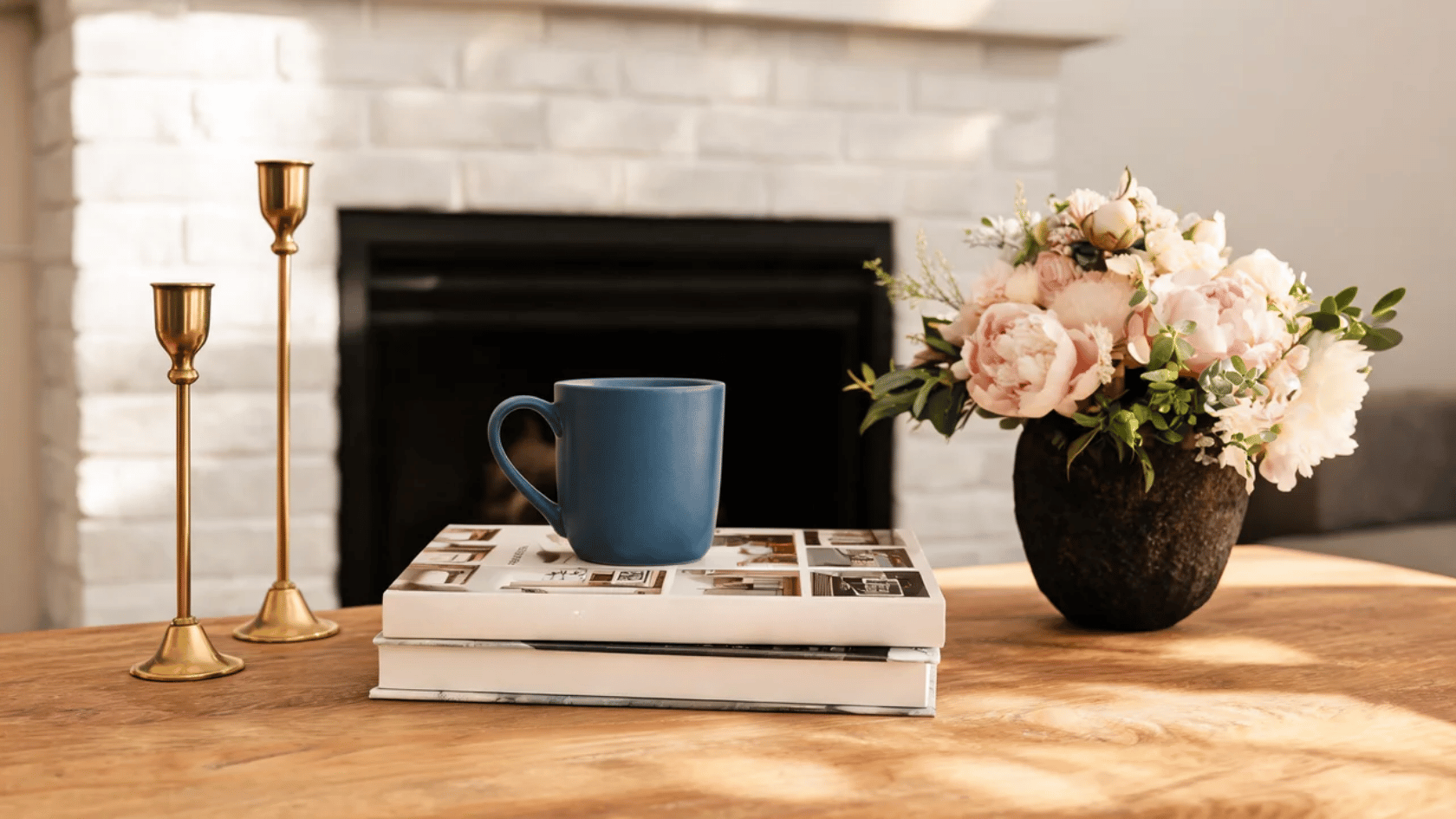 Nancy Meyers aesthetic vignette with a cozy fireplace, coffee mug, flowers, and warm decor.