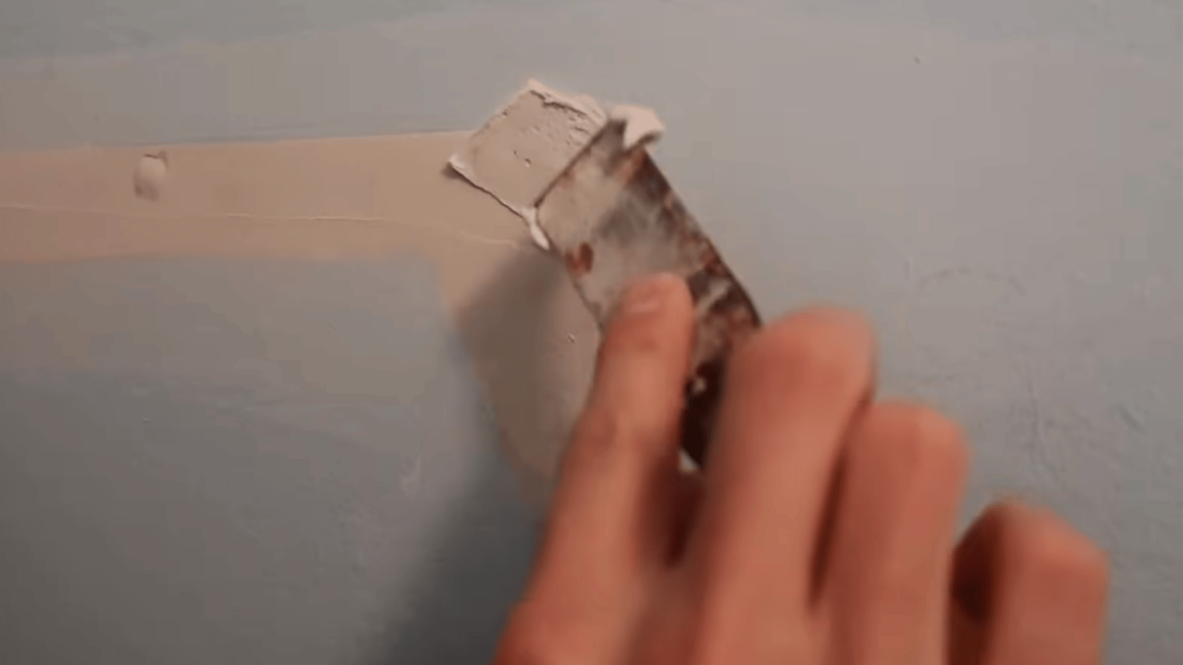 Hand applying a second layer of drywall compound over a patched wall hole with a putty knife.