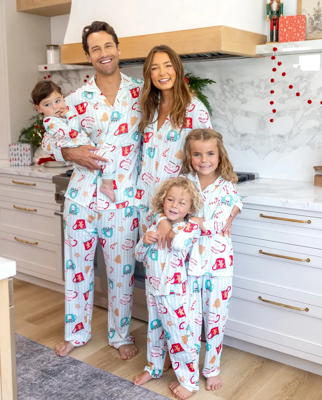 Family in matching holiday pajamas smiling in modern kitchen with marble backsplash