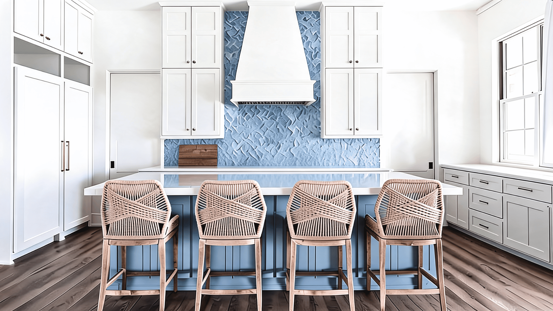 Coastal white kitchen with blue island, blue kitchen wall, woven seats, glass backsplash, sleek shaker cabinets, and wood flooring.