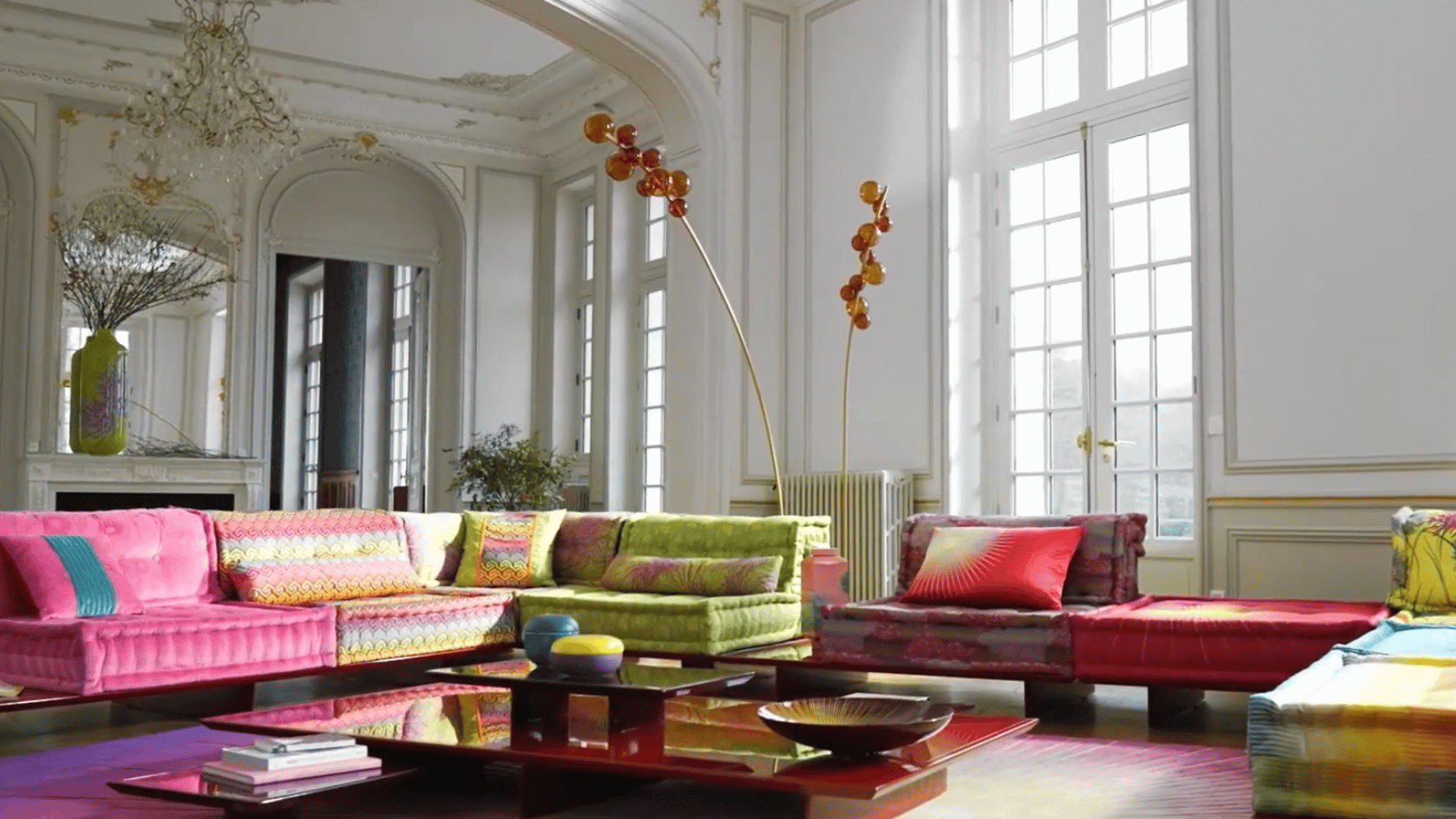 Colorful living room with vibrant sofas, large windows, ornate architecture, and eclectic modern decor.