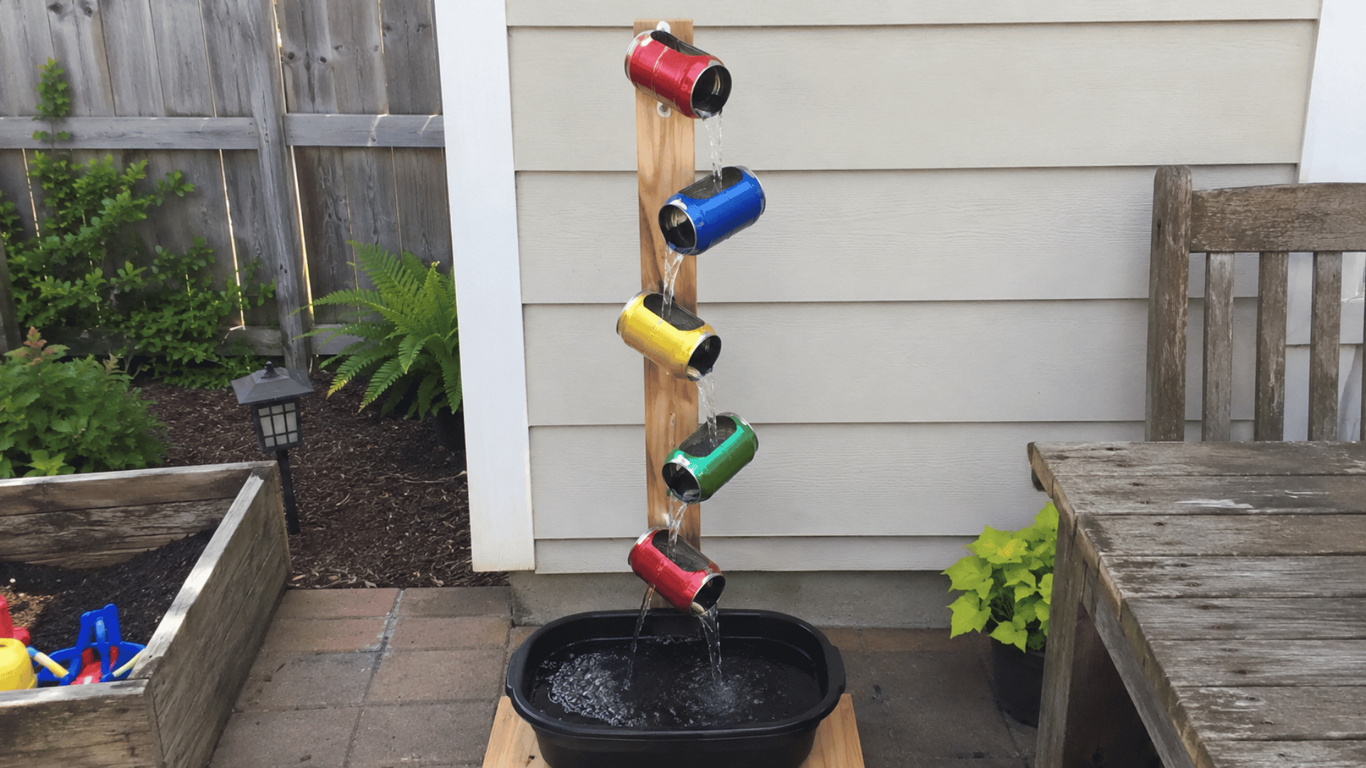 colorful soda cans mounted vertically pouring water into black basin on patio