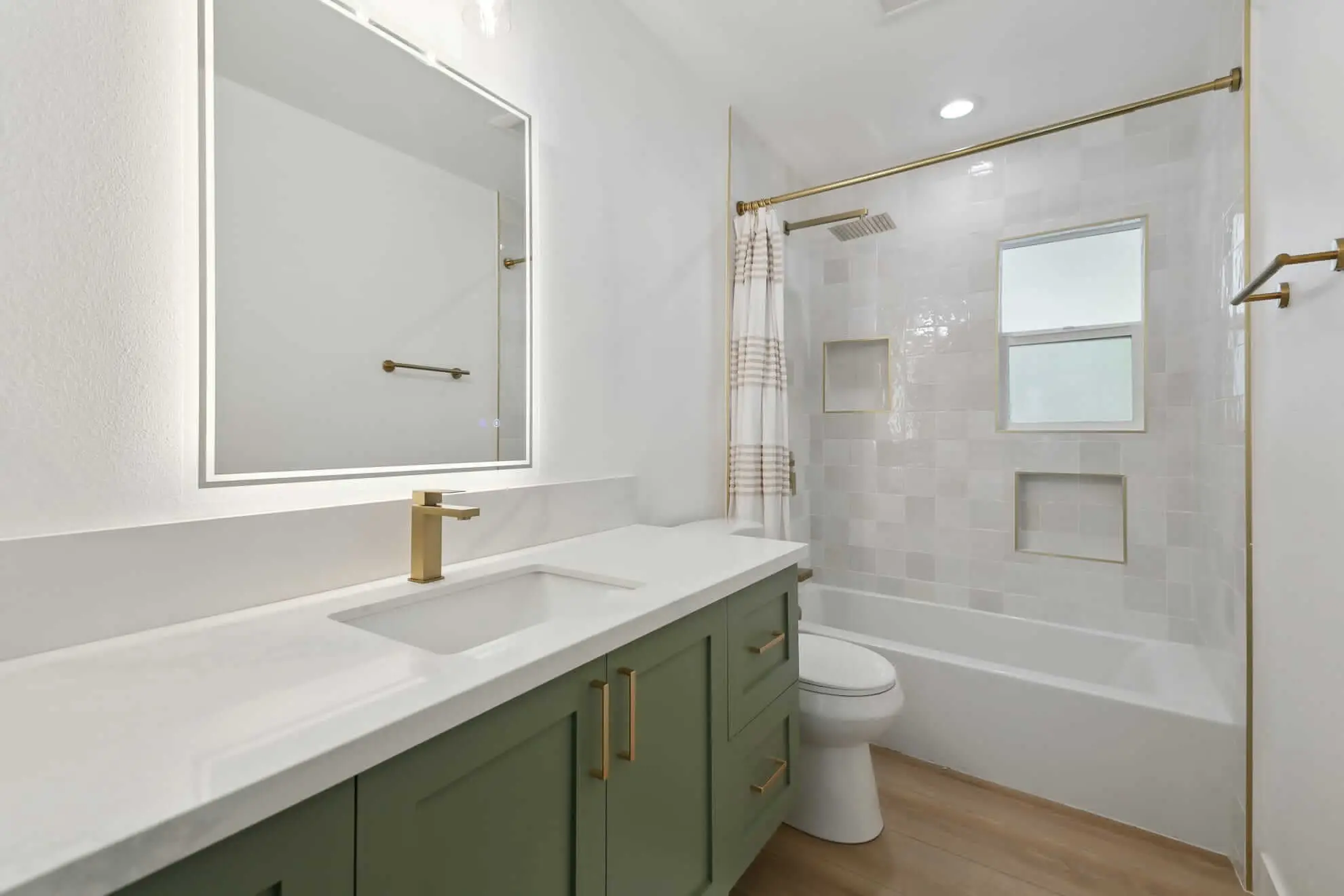 Modern bathroom with green vanity, gold fixtures, white countertop, and tiled shower with brass accents