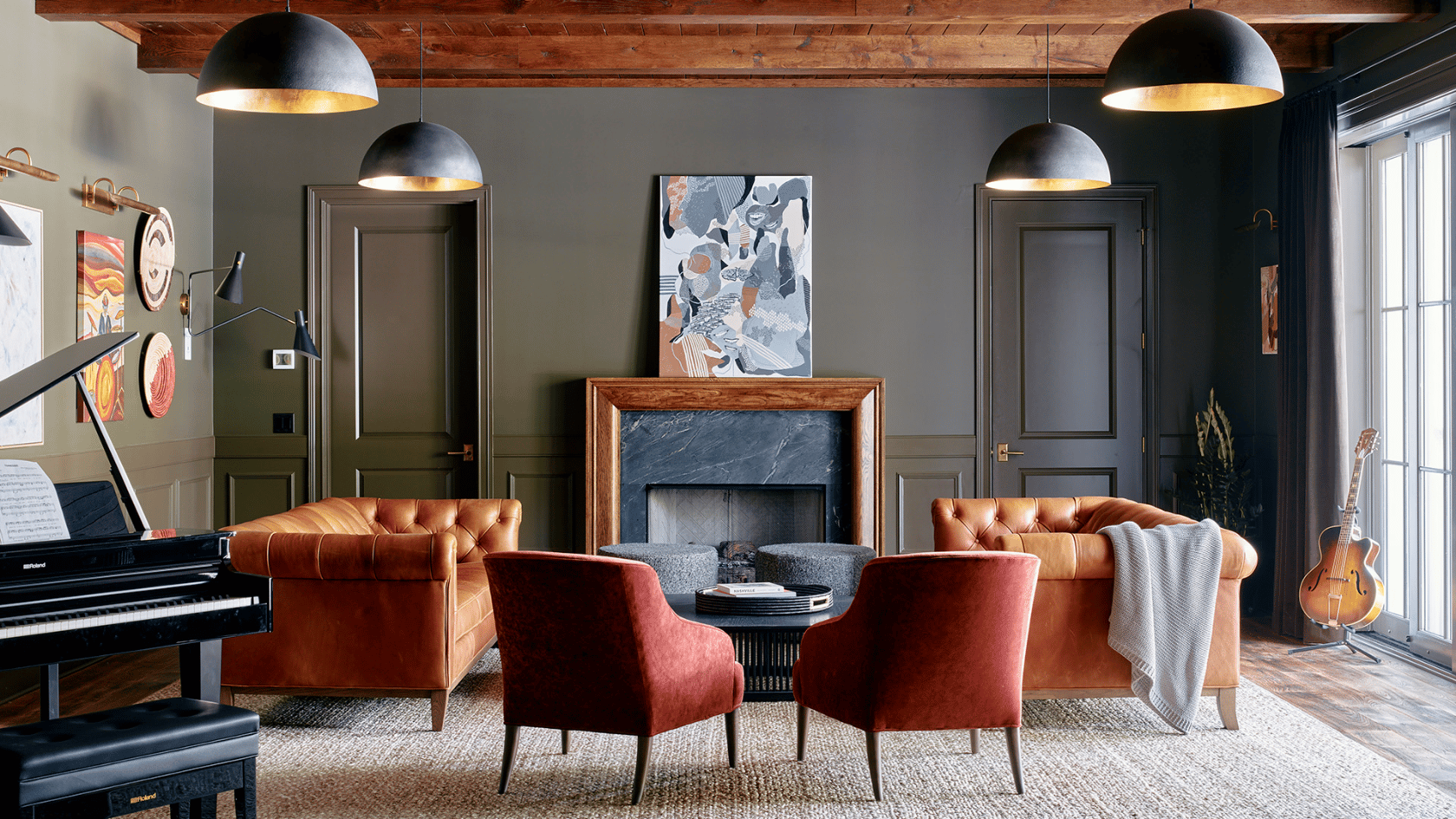Dark moody living room with leather sofas, velvet chairs, fireplace, piano, and warm pendant lighting.