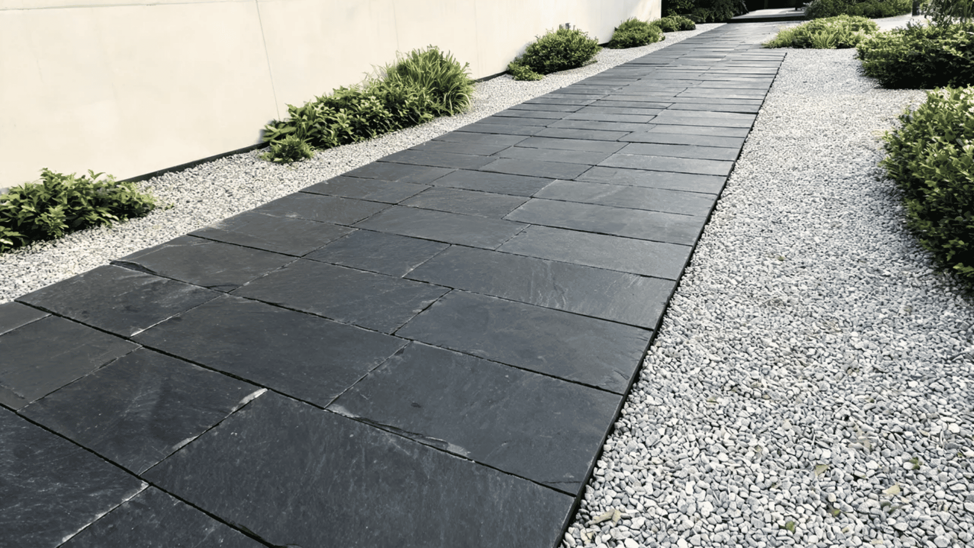 Dark slate stone walkway bordered by gravel and green plants in a modern landscape.