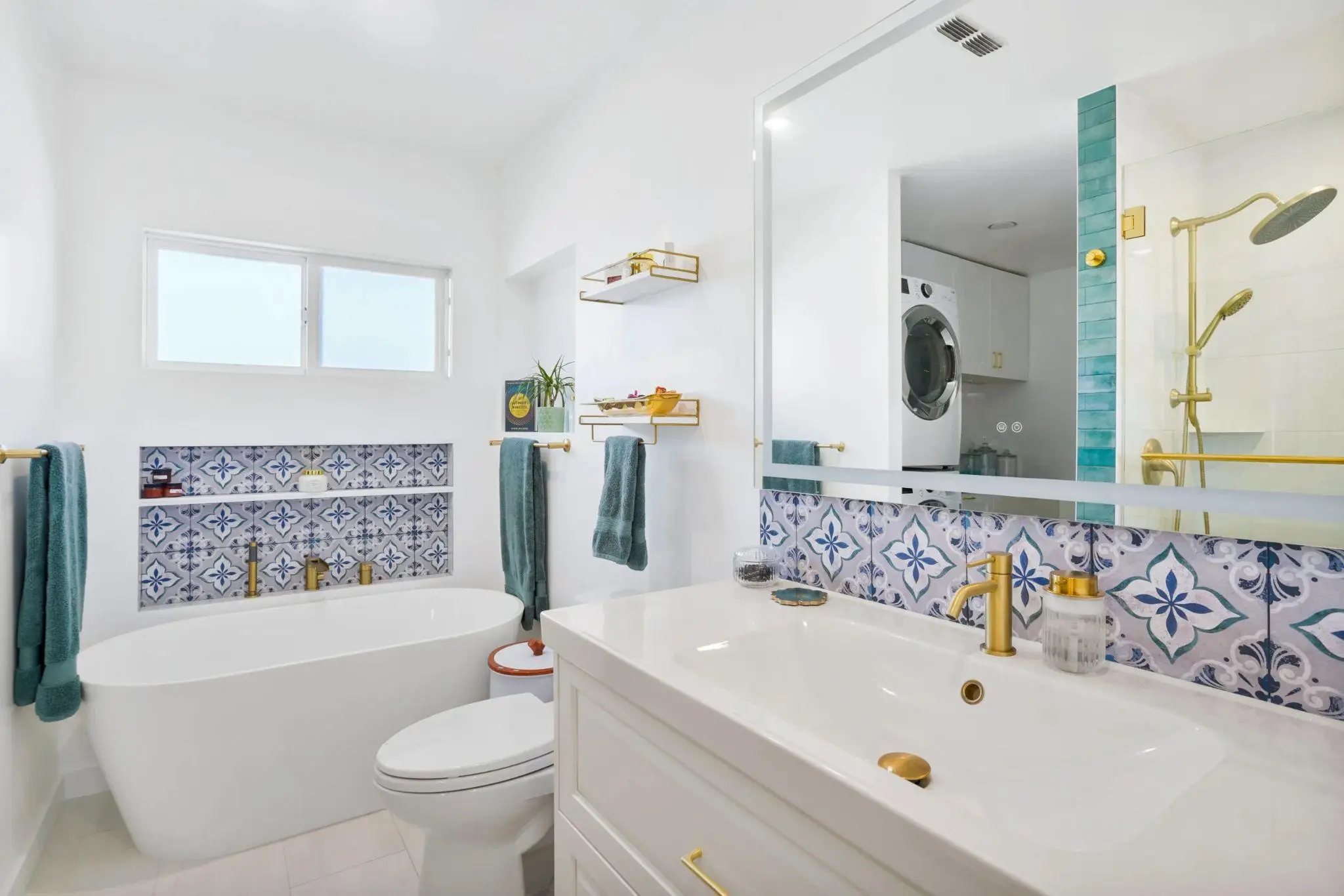 Modern bathroom with freestanding tub, patterned blue tiles, gold fixtures, and teal towels