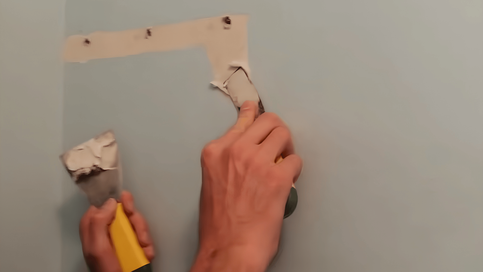 Hands applying drywall compound to a wall hole with a putty knife during repair