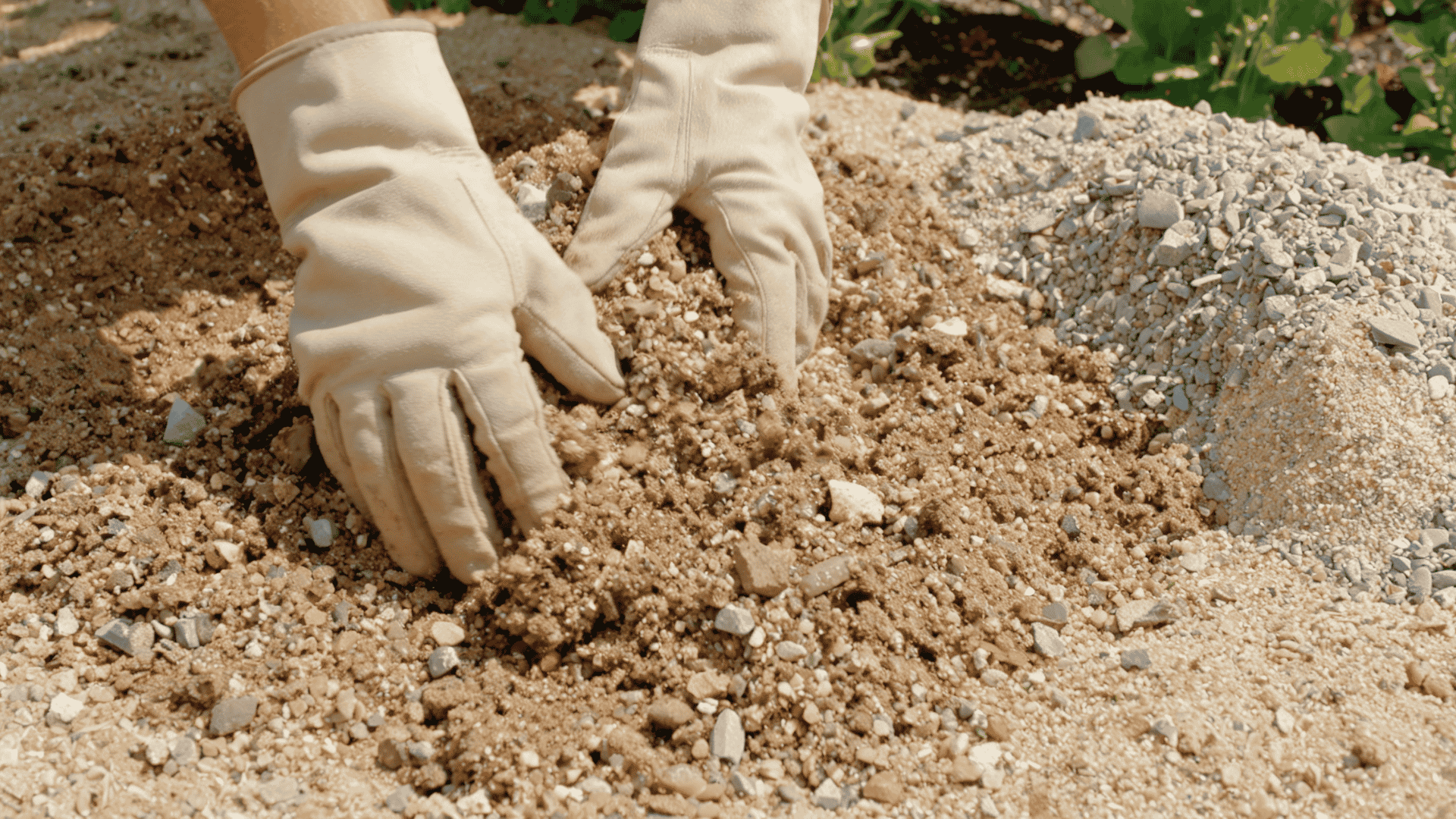 Gloved hands mixing sand and gravel into garden soil to create loose, well-draining soil for lavender