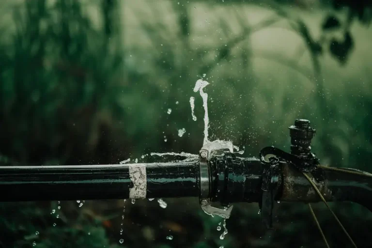 Leaking black pipe with dripping water in outdoor lush green setting