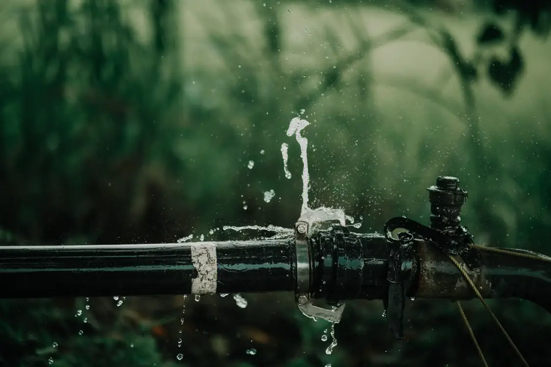 Leaking black pipe with dripping water in outdoor lush green setting