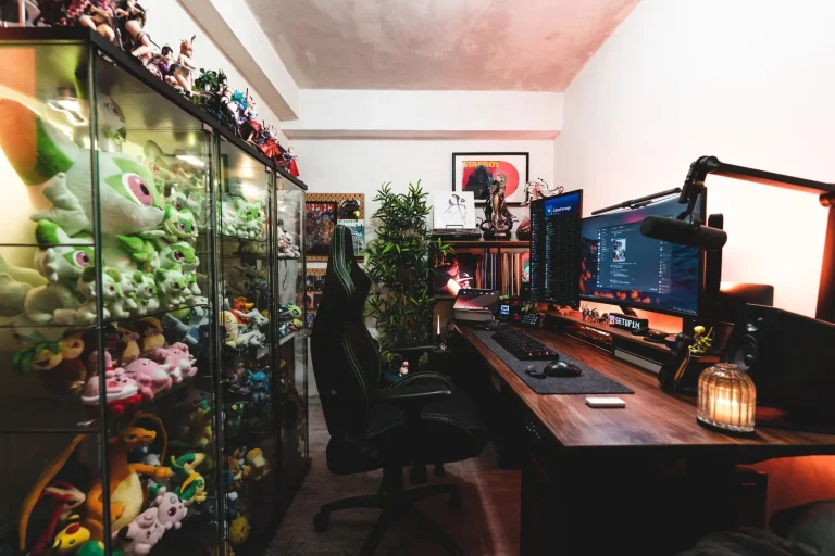 Gaming setup with dual monitors and plush toys in a cozy room with warm lighting