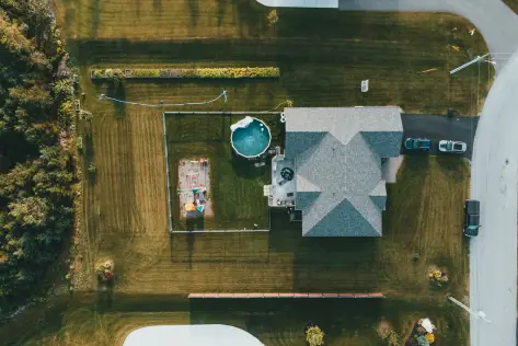 Suburban house with swimming pool and play area in green grassy yard, aerial view