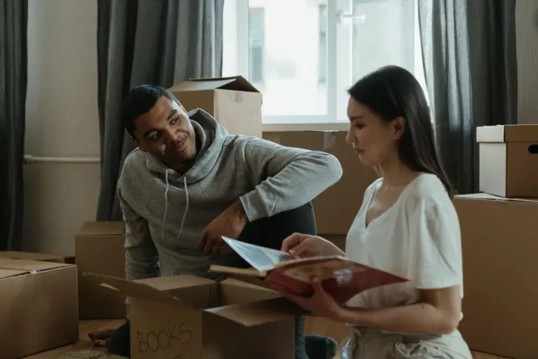Couple unpacking boxes and reading book in sunlit room with curtains
