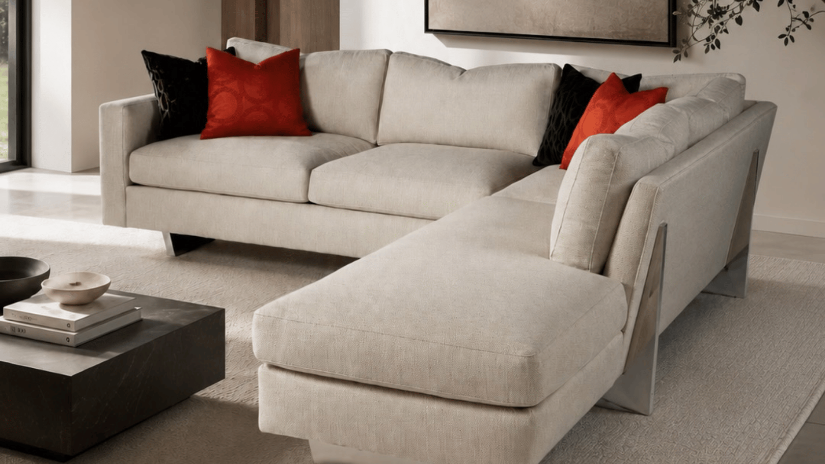 Modern living room with cream sectional sofa, black coffee table, red accent pillows, and minimalist decor.