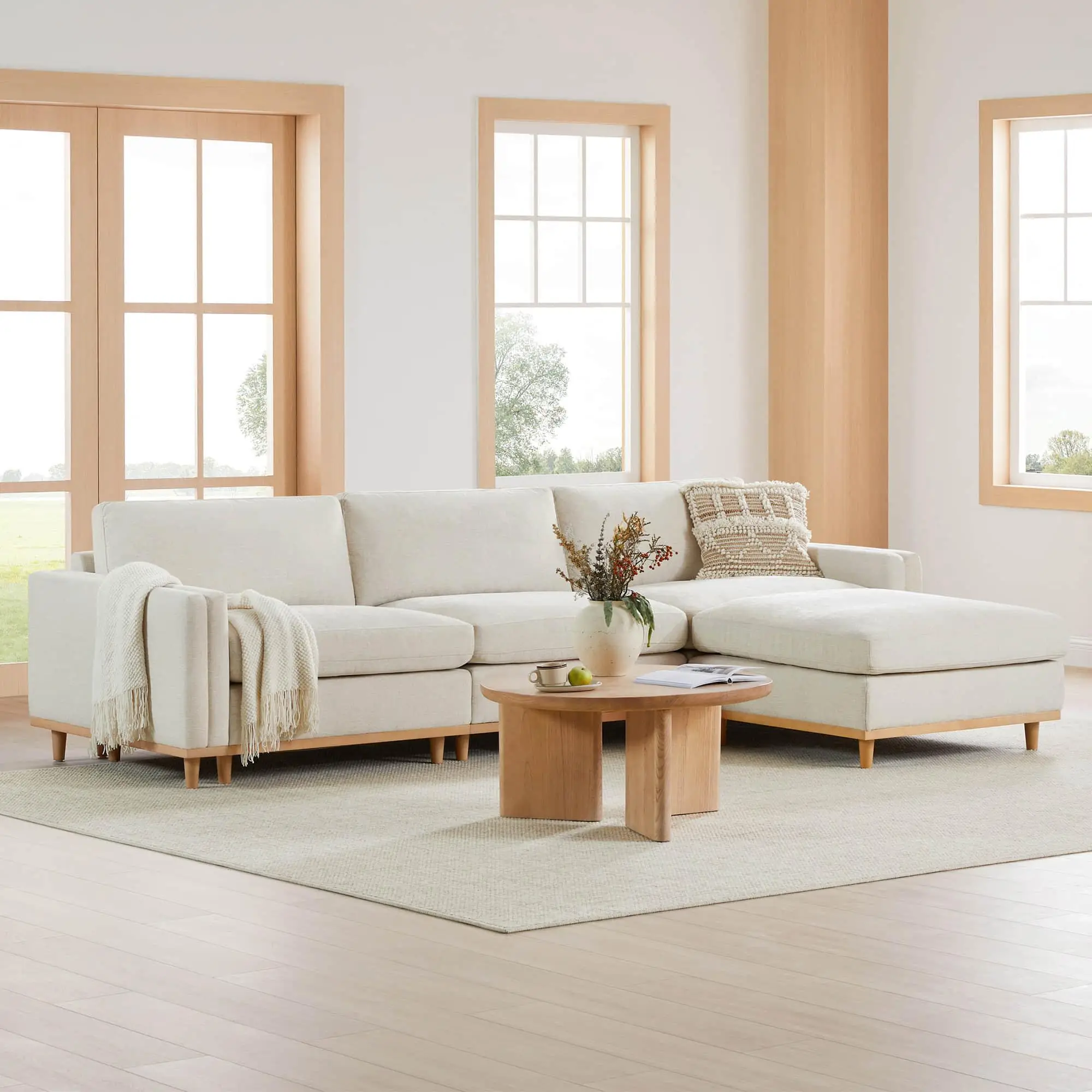 Beige sectional sofa with textured pillows and blanket in bright living room with wooden coffee table