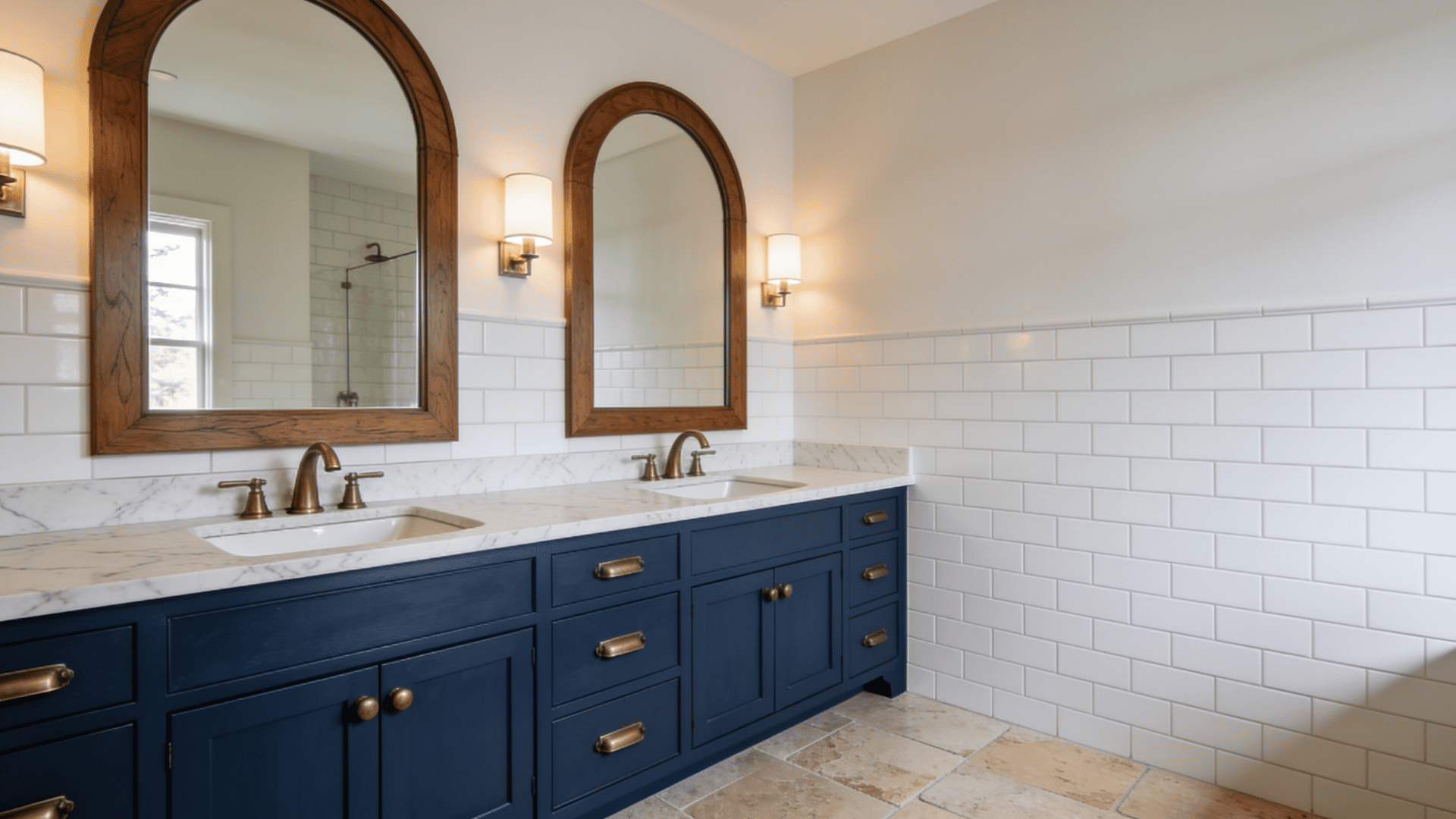 Navy double vanity with marble counters, arched wood mirrors, brass fixtures, and white subway-tiled walls.