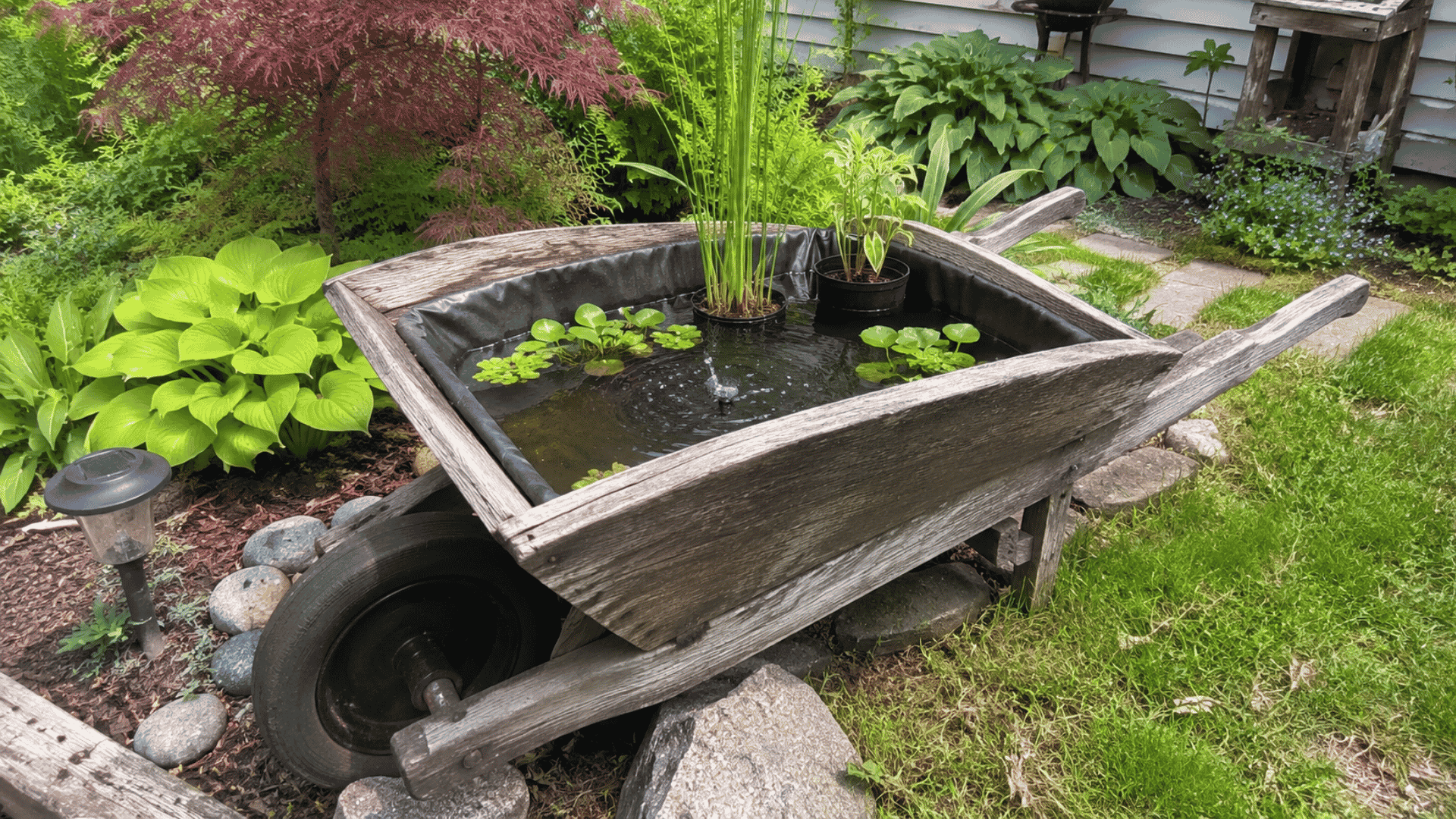 old wooden wheelbarrow lined pond with potted plants and small fountain outdoors