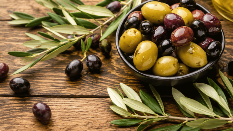 Bowl of mixed olives with olive branches and oil on a rustic wooden table.