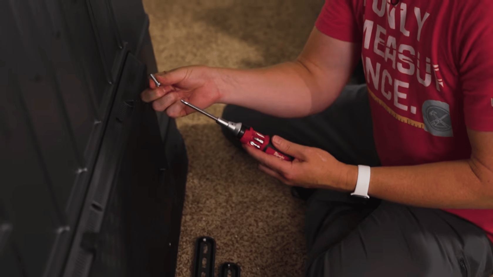 Person attaching mounting brackets to the back of a TV using a screwdriver during installation.
