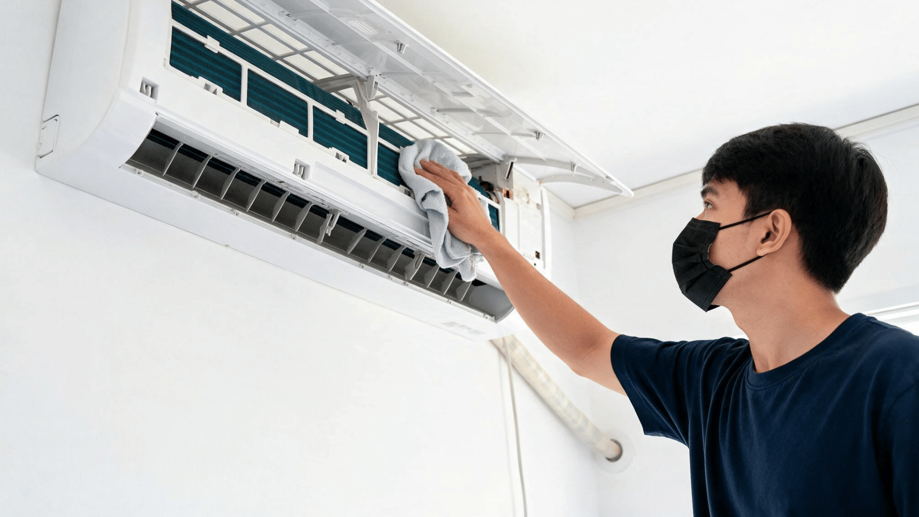person cleaning an indoor air conditioner unit with a cloth as part of routine home ac maintenance and care