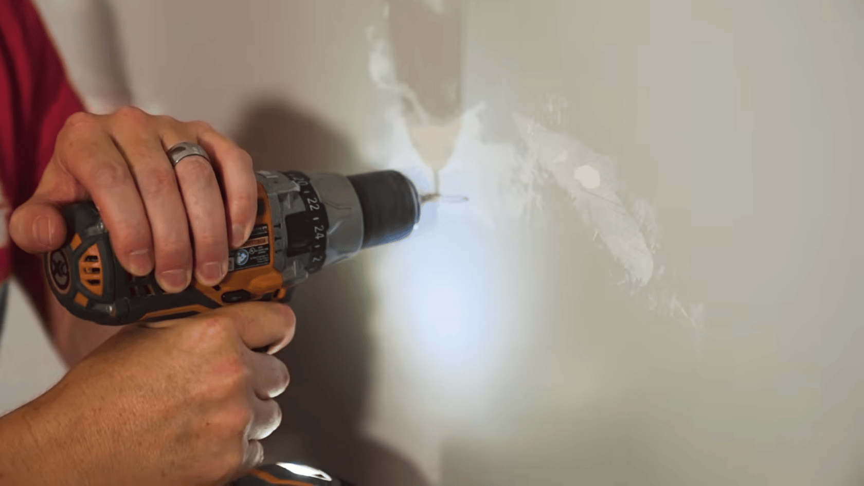 Person drilling pilot holes in a wall for TV mount installation.