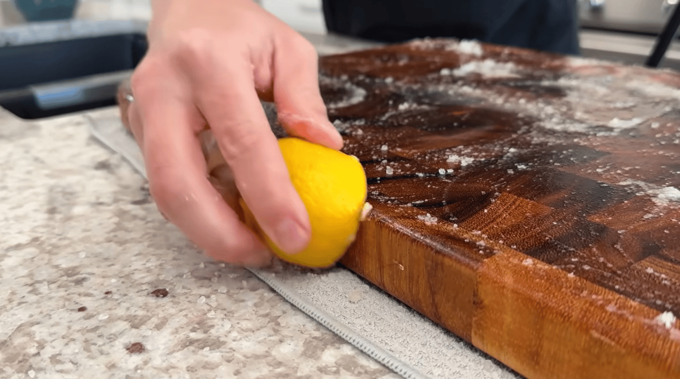 person rubbing lemon on a wooden cutting board with salt for removing odors and surface residue