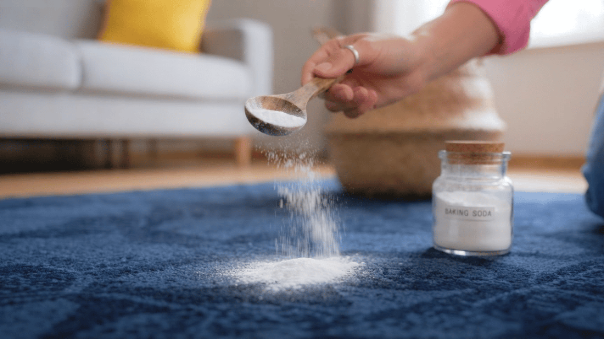 Person sprinkling baking soda on a blue carpet for odor removal
