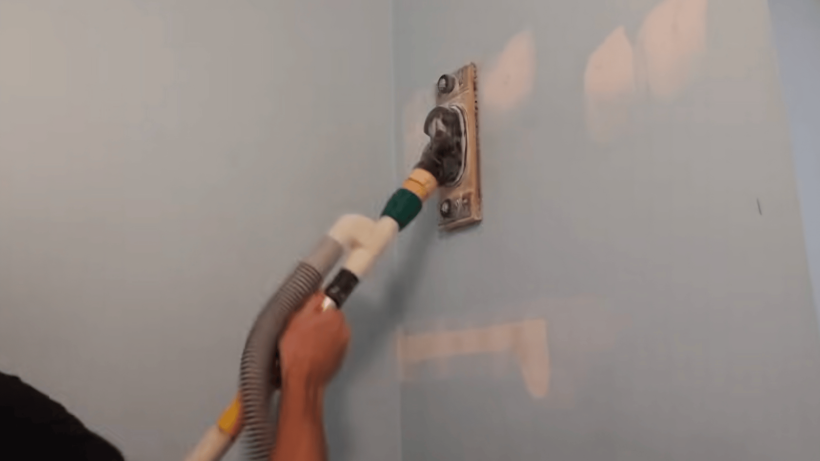 Person sanding a patched drywall anchor hole with a sanding tool to smooth the repair