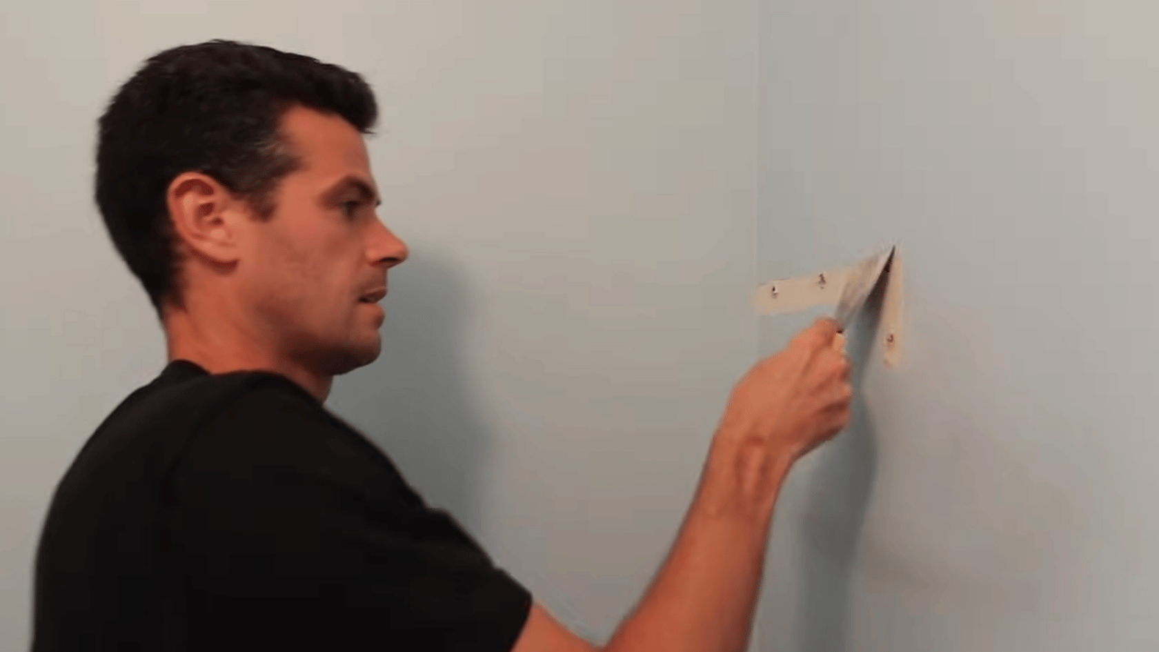 Person scraping loose material from a drywall hole with a putty knife before repair