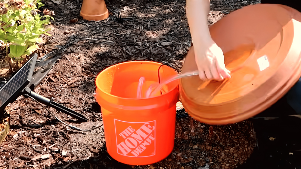 person connecting clear tubing between an orange bucket and terracotta saucer for a diy bird bath fountain