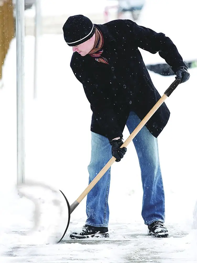 Person shoveling snow on pavement wearing warm clothing and gloves in winter setting