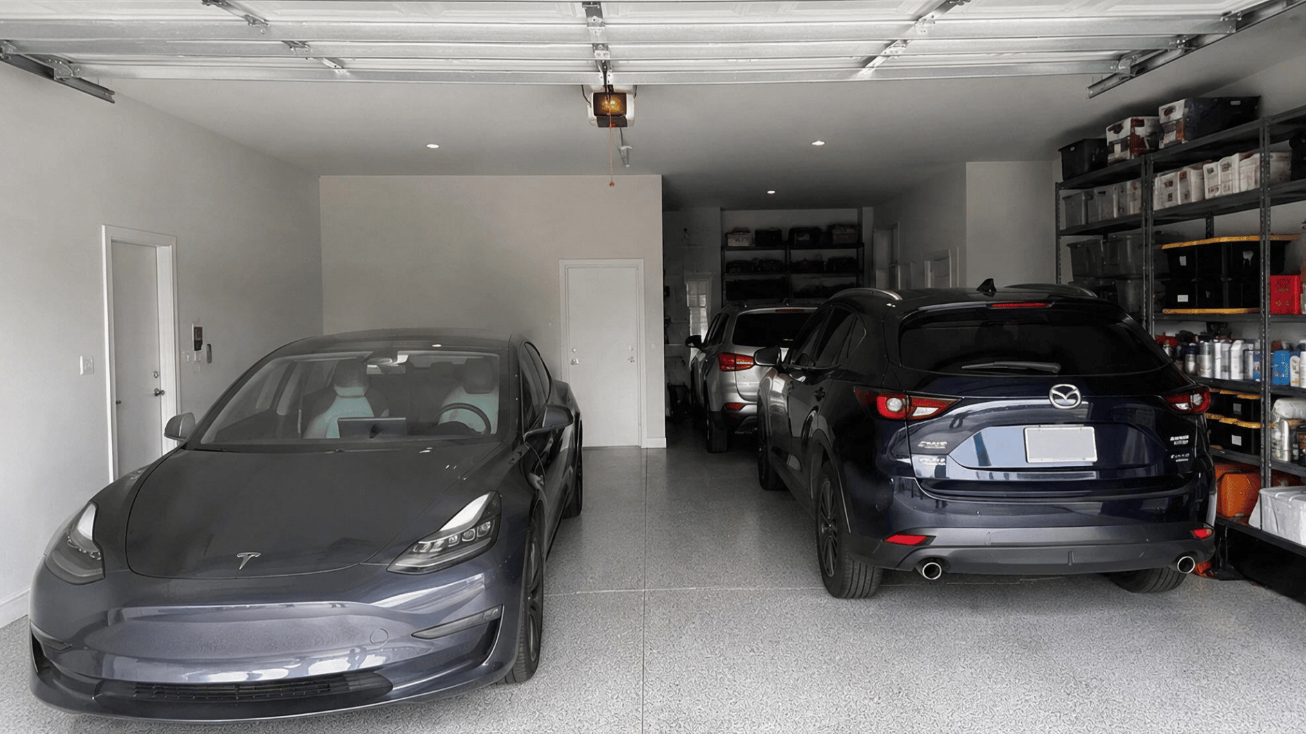 three cars parked inside an organized garage with storage shelves white walls and a smooth gray finished floor