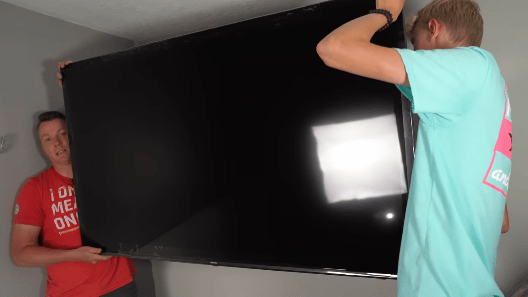 Two people lifting a TV onto a wall mount to complete the installation process.