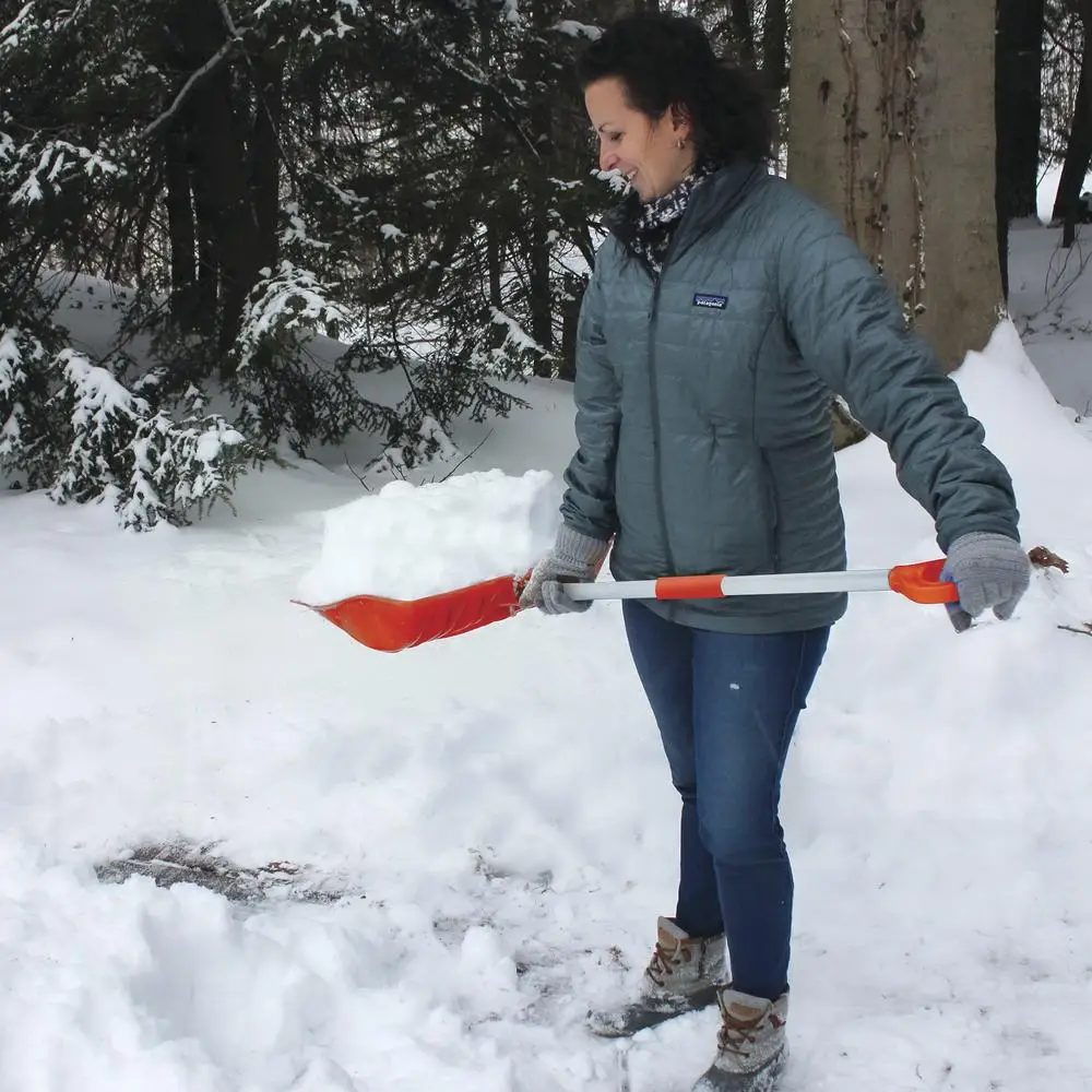 Person shoveling snow with orange shovel in snowy forest setting
