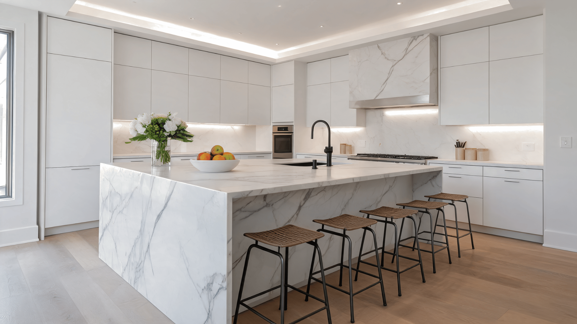 White kitchen with waterfall island, veined stone countertop, modern cabinets, bar seating, and a seamless sculptural design.