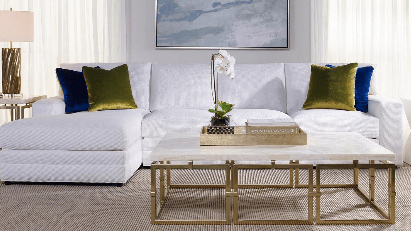 White sectional sofa with blue and green accent pillows, marble coffee table, and modern neutral living room decor.