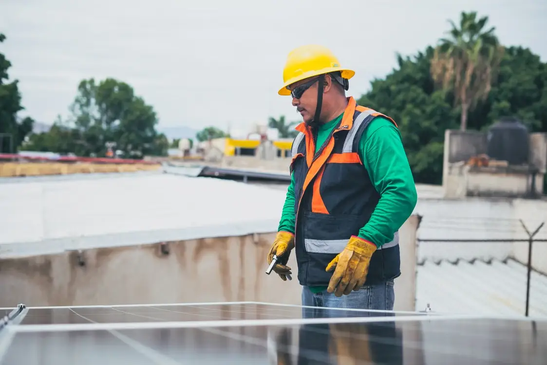 Worker in safety gear inspecting solar panels on an outdoor rooftop