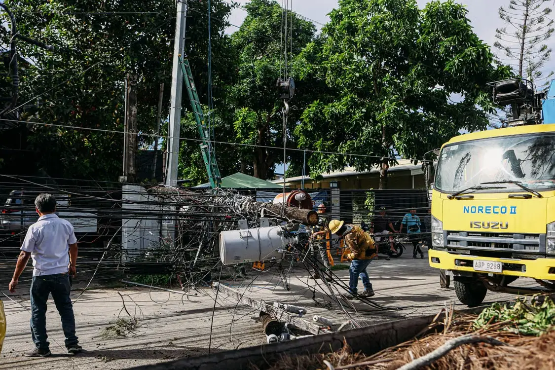 Utility workers repairing fallen power lines on a street with yellow truck nearby