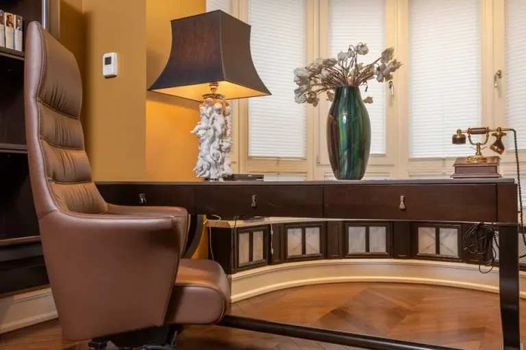 Brown leather office chair at dark wood desk with lamp and decorative vase in cozy room