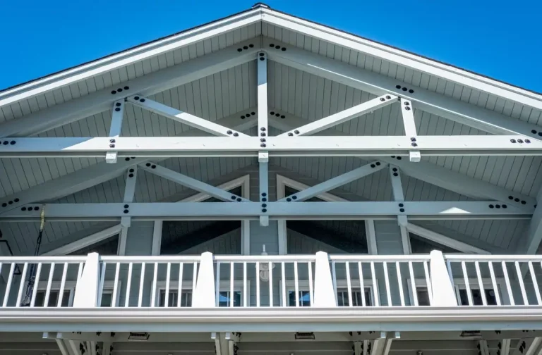 White wooden gable roof with exposed beams and balcony railing under clear blue sky