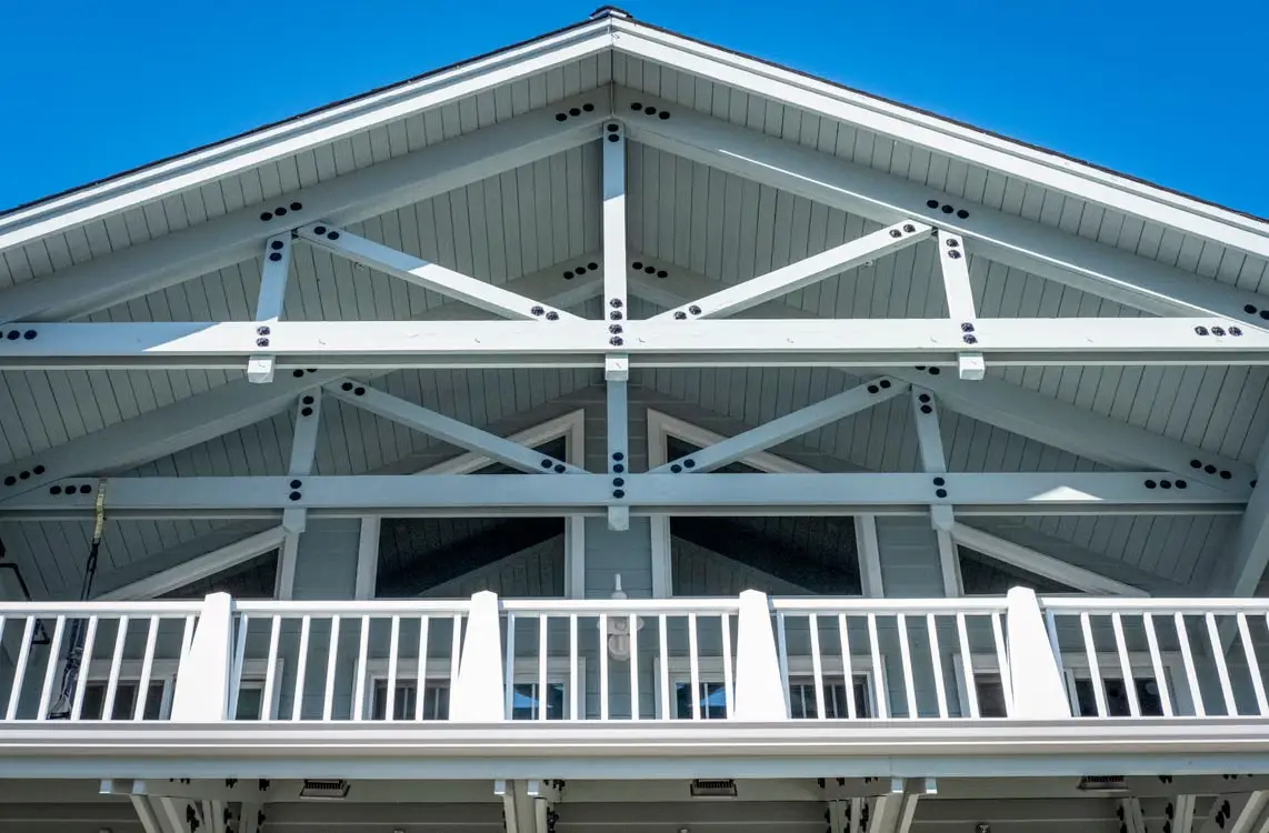 White wooden gable roof with exposed beams and balcony railing under clear blue sky