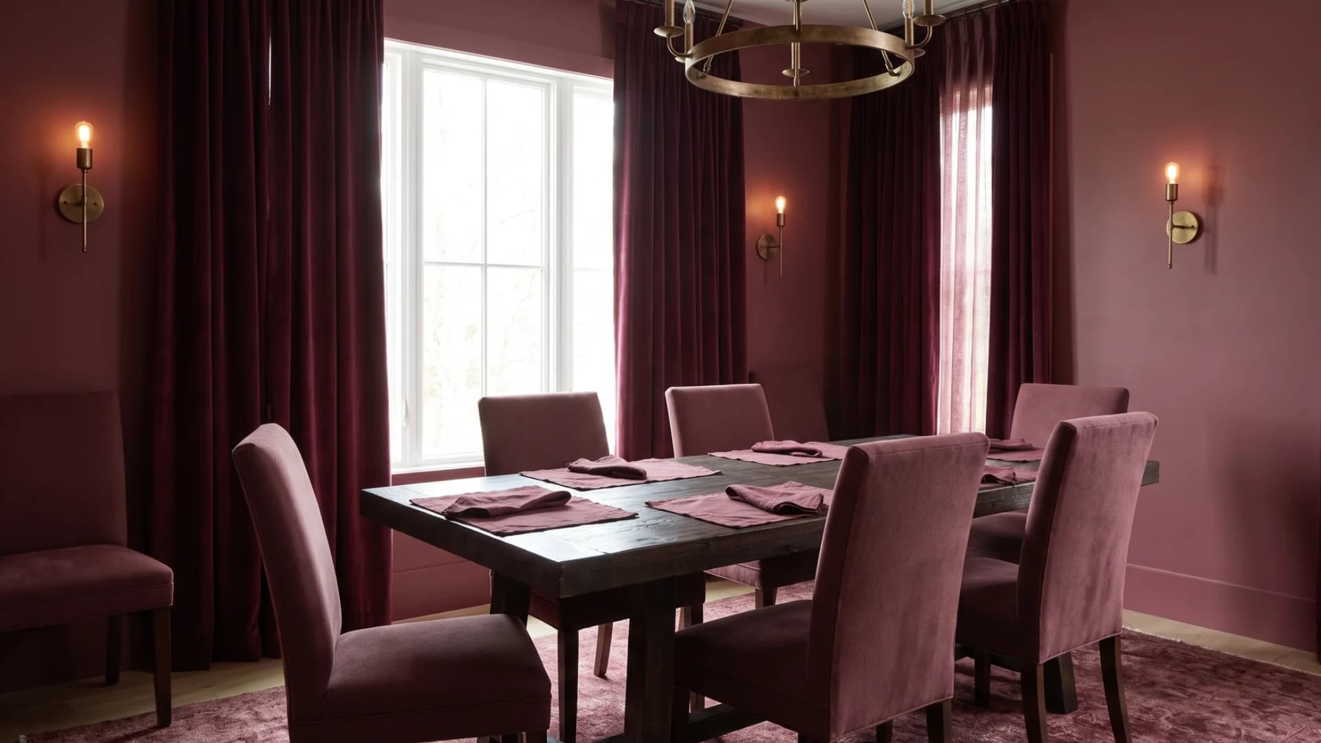 Deep burgundy dining room with a dark wood table and brass lighting fixtures.