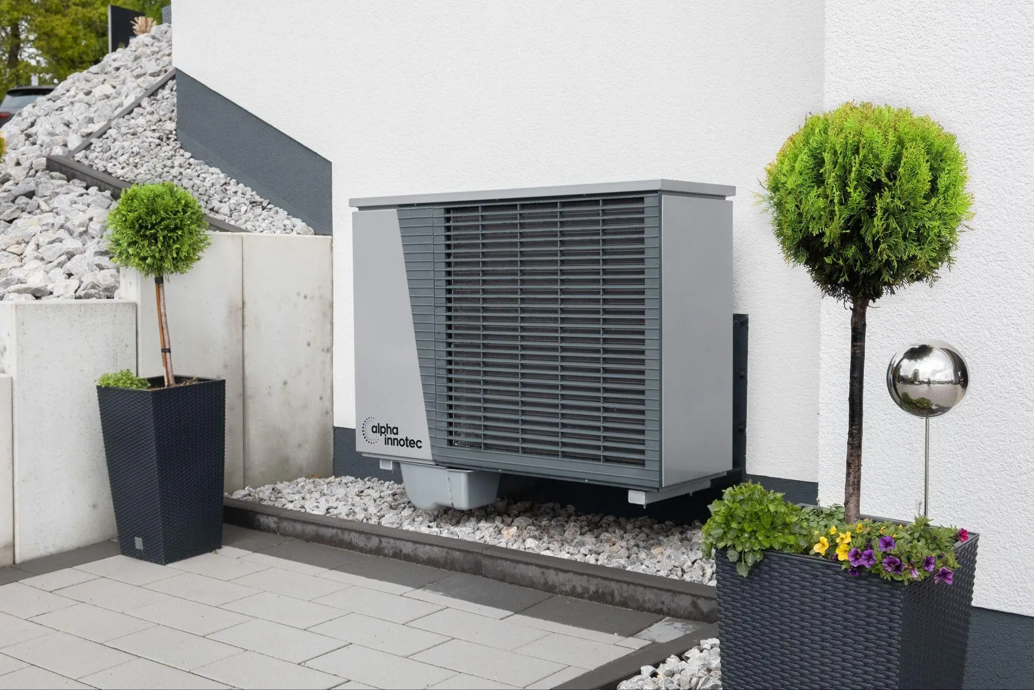 Outdoor heat pump unit on concrete patio with decorative potted plants and gravel landscaping