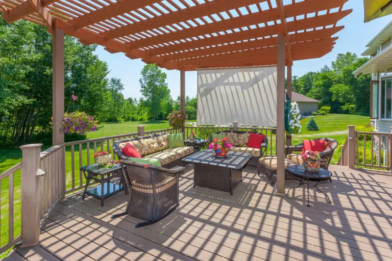 Outdoor patio with wicker furniture and vibrant cushions under wooden pergola in sunny garden setting