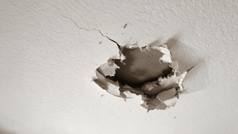 cracked and damaged drywall ceiling with a hole exposing gypsum board