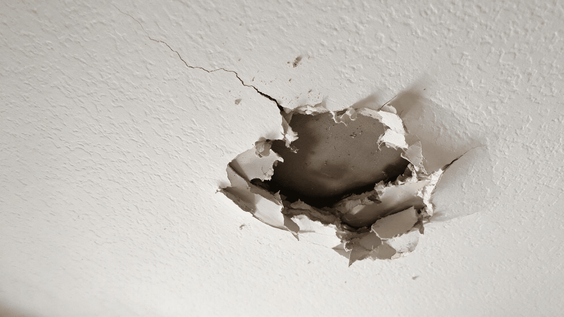 cracked and damaged drywall ceiling with a hole exposing gypsum board