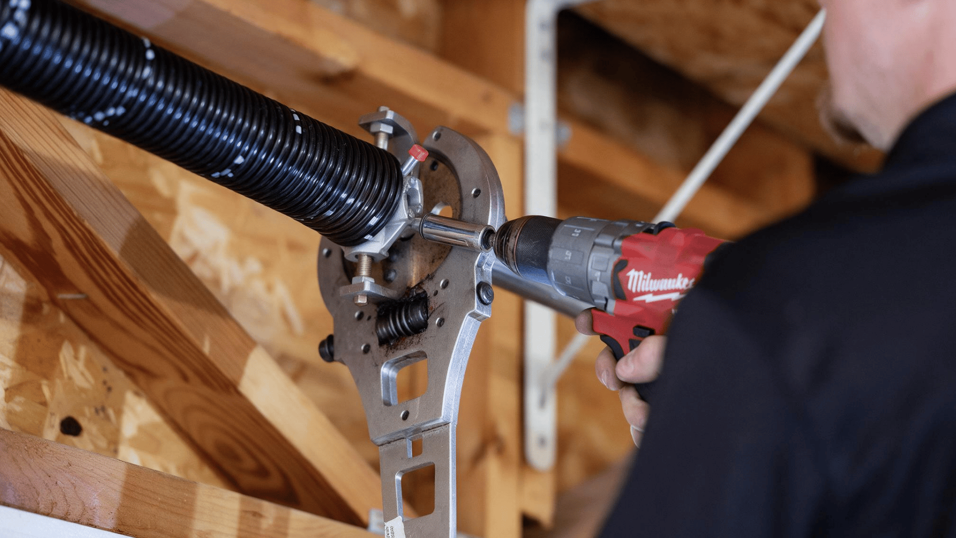 technician using a power drill on garage door torsion spring hardware during repair or replacement work