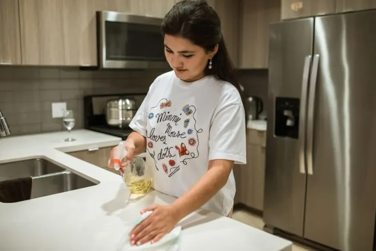 Woman wiping kitchen counter with cleaning spray in modern kitchen setting