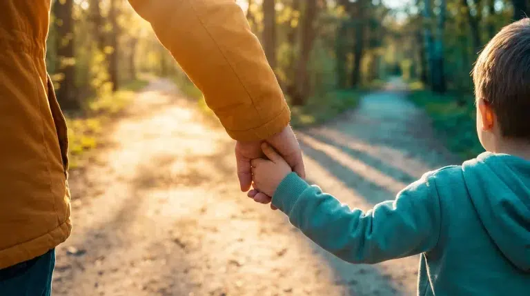 Adult and child holding hands on sunlit forest path